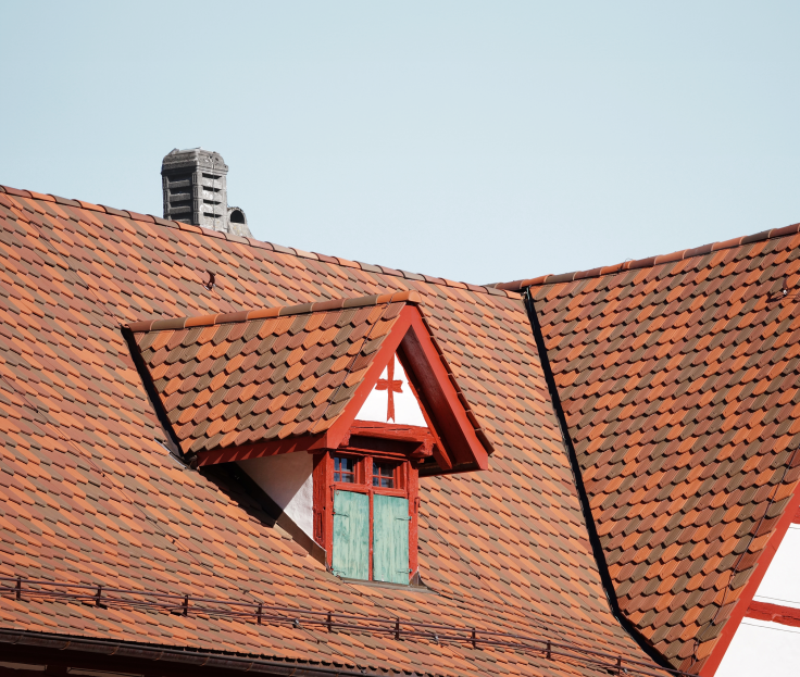 Rotes Ziegeldach mit kleinem Dachfenster und blauer Himmel im Hintergrund.