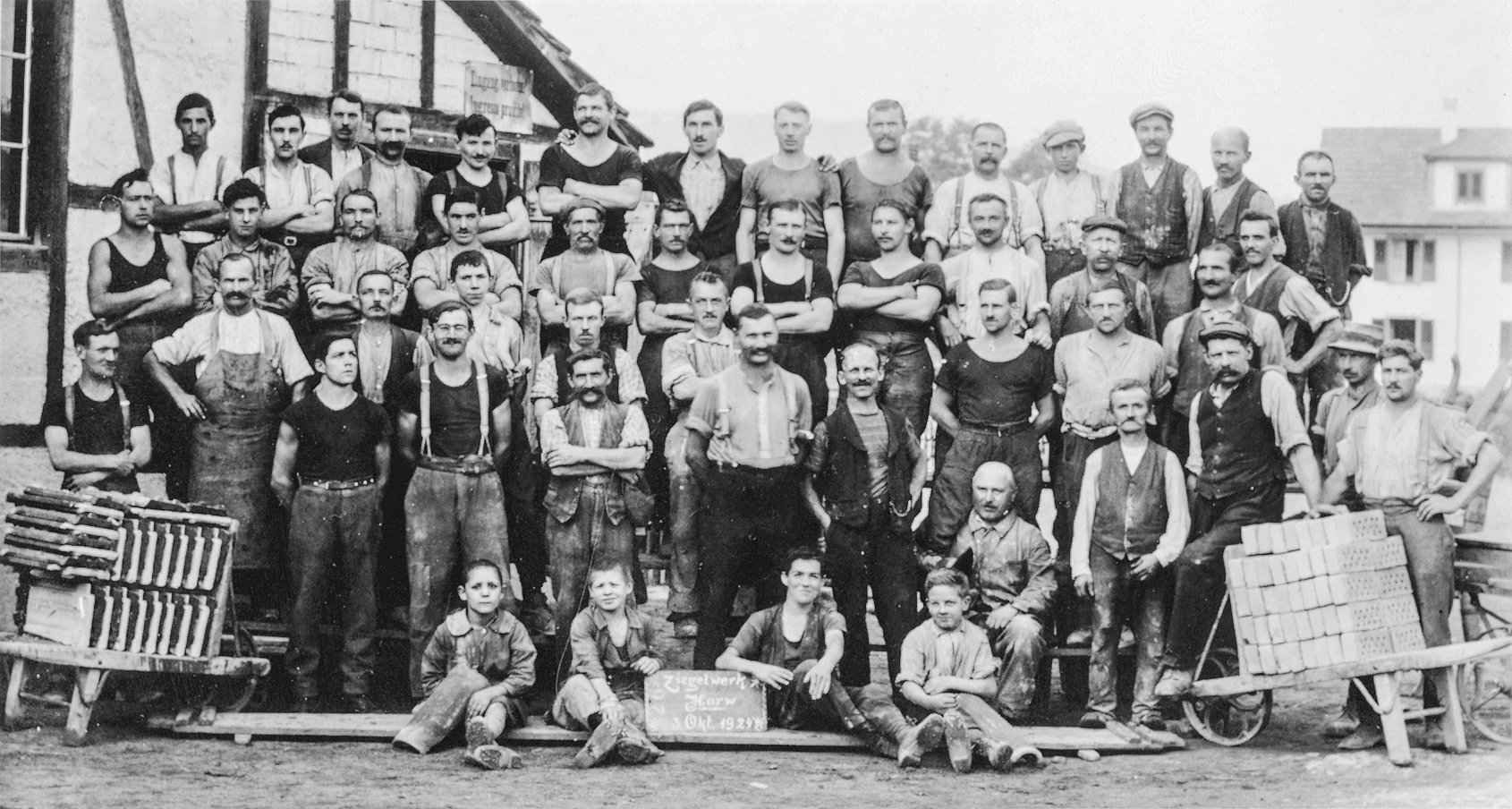 Schwarzweissfoto einer grossen Gruppe von Arbeitern vor einem Fachwerkhaus.