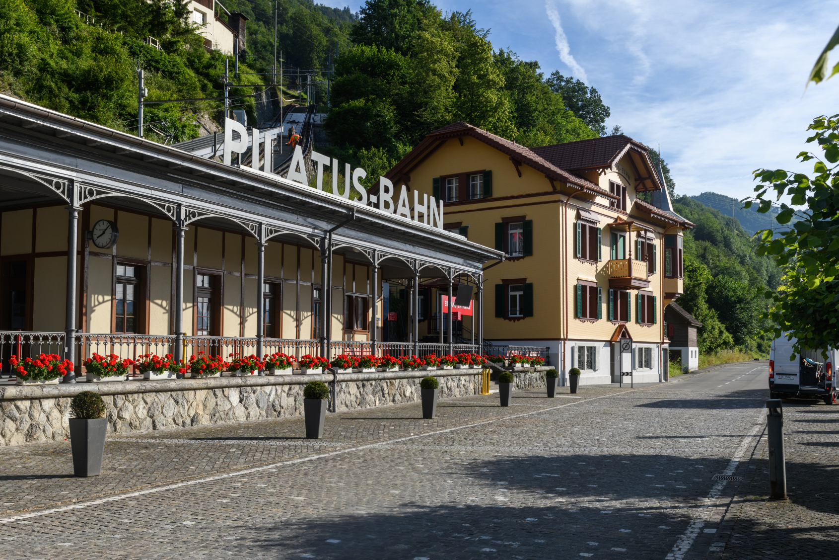 Bahnhof Pilatusbahn mit Blumen und historischem Gebaude vor bewaldetem Hang