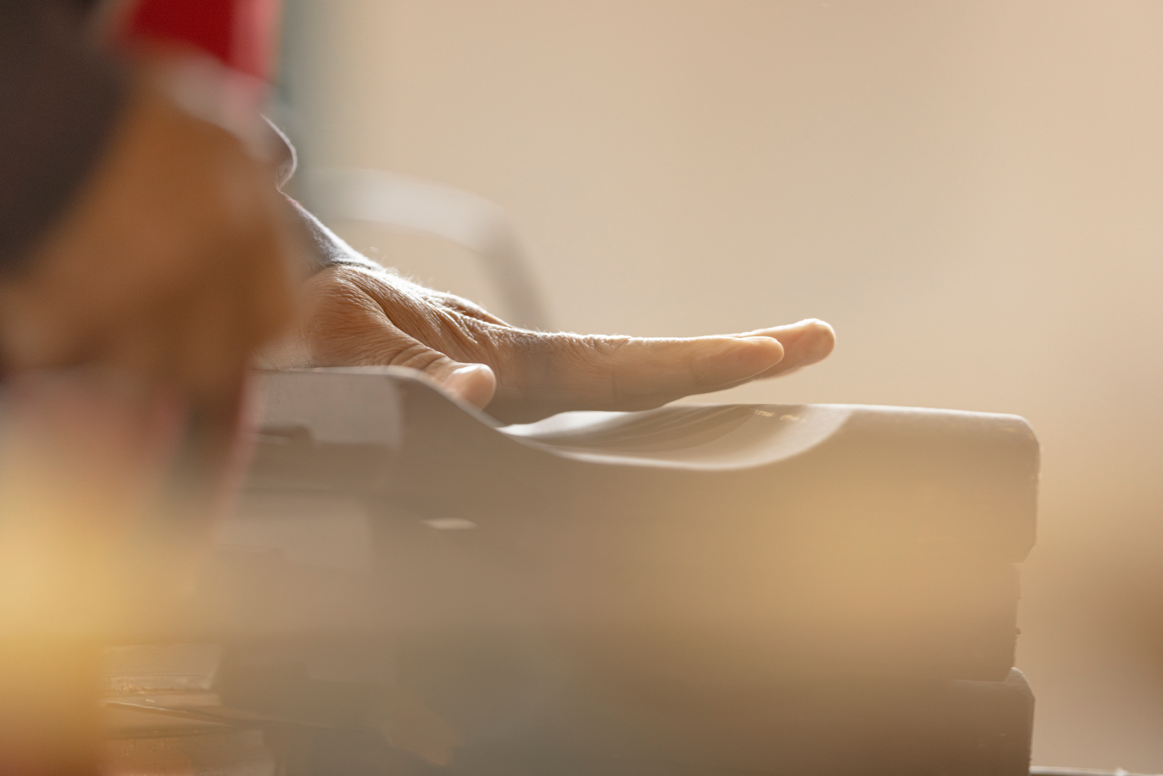 Hand legt sich auf einen Dachziegel, unscharfer Hintergrund, warmes Licht